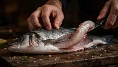A fillet knife sliding along the backbone of a fresh fish on a wooden board, lifting a clean fillet away.